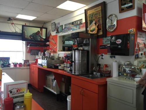 A cozy diner interior with orange counters, a coffee machine, and vintage decor, including signs and a TV.