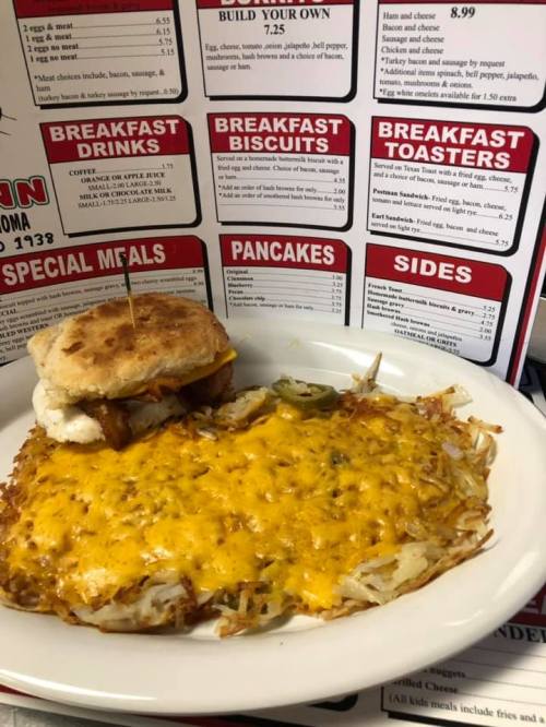 A plate with a cheesy breakfast sandwich and golden hash browns, next to a menu board featuring various breakfast options.