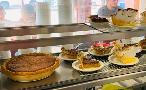 A display of various pies, including a large pie and several slices on plates, in a bright, casual setting.