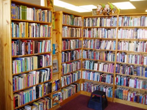 A cozy corner of a library with wooden shelves filled with colorful books and a small stool in front.