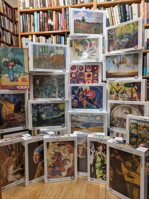 A collection of jigsaw puzzle boxes featuring famous artworks, displayed in a cozy library setting.