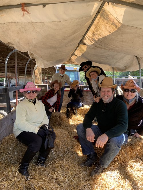A group of eight people in cowboy hats sitting on hay bales inside a barn, smiling and enjoying their time together.