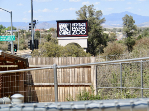 Sign for Heritage Park Zoo visible in the background, with a fenced area in the foreground and mountains in the distance.