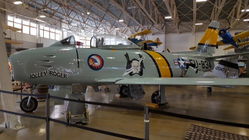 A vintage aircraft with a light green body, featuring a Native American emblem and a pirate logo, displayed indoors.