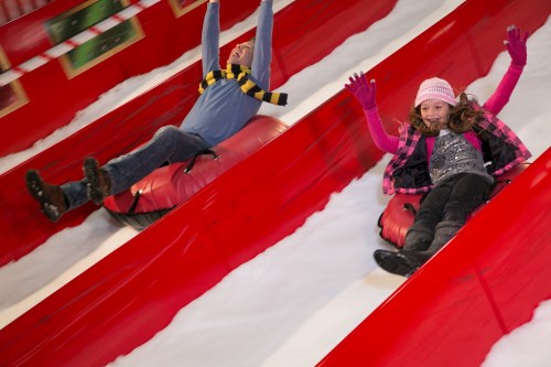 A man and a girl slide down a snowy slope on inflatable tubes, both smiling and enjoying the winter fun.