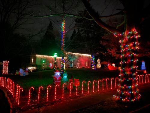 A festive house decorated with colorful Christmas lights and inflatable decorations, including snowmen and candy canes.