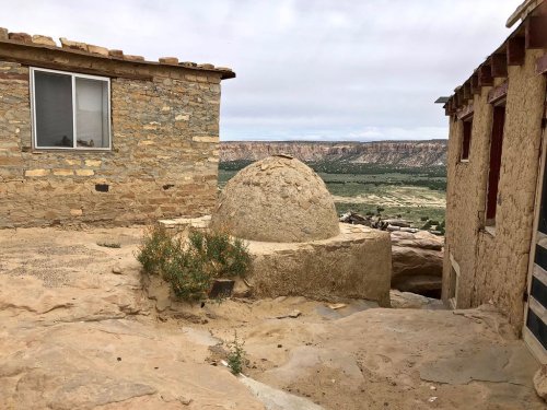 A stone structure with a dome sits between two buildings, overlooking a vast landscape with cliffs in the background.