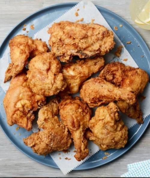 A blue plate filled with crispy fried chicken pieces, arranged on parchment paper.