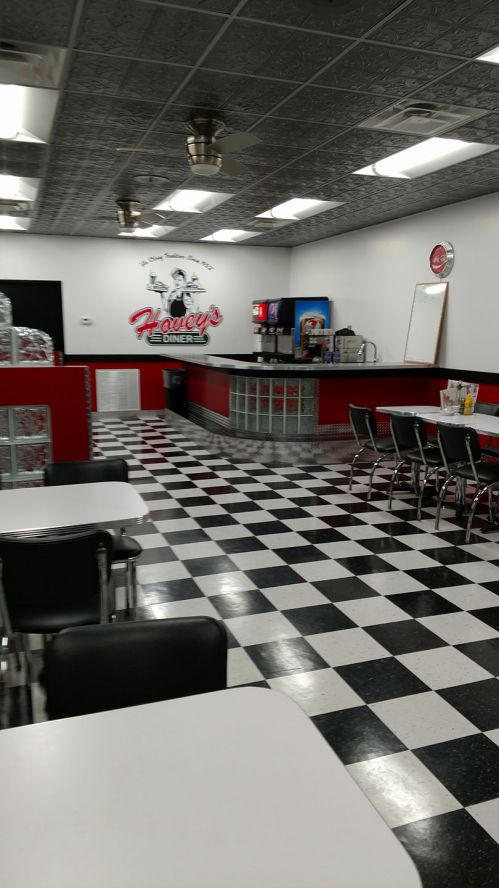 Interior of a diner with a checkered floor, red and black decor, and a counter with drink dispensers.