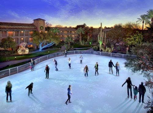 A festive outdoor ice skating rink with people skating, surrounded by palm trees and holiday decorations at sunset.