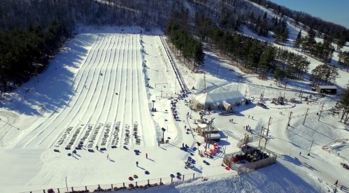 A snowy landscape with multiple tubing lanes, a large tent, and people enjoying winter activities.