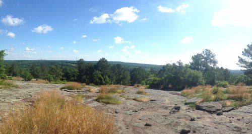A panoramic view of a rocky landscape with green trees and blue skies dotted with clouds.