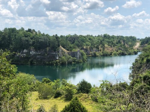 A serene lake surrounded by lush greenery and rocky cliffs under a partly cloudy sky.