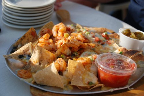 A platter of shrimp nachos topped with cheese, tomatoes, and served with salsa and jalapeños on the side.