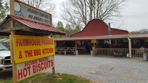 A rustic building with a sign for "Farmhouse Produce & The BBQ Kitchen" and "Home Made Hot Biscuits" in a gravel lot.
