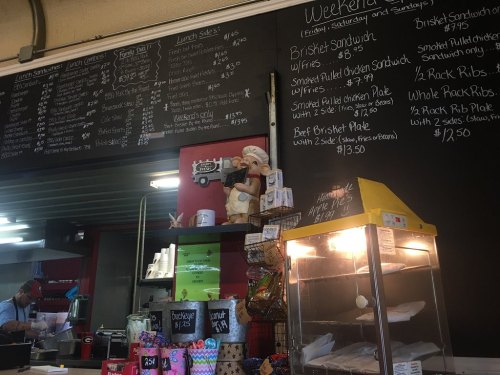 A chalkboard menu displays lunch options at a restaurant, with a decorative chef figure and a food display case in view.