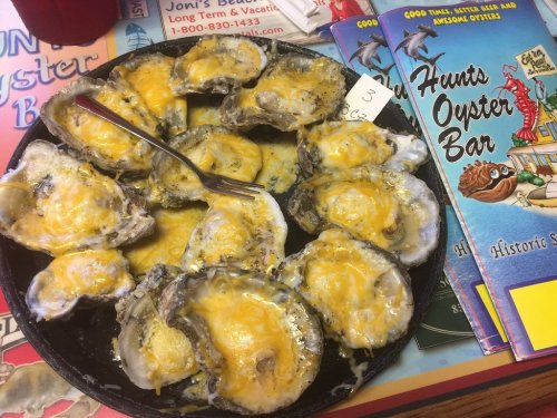 A plate of baked oysters topped with melted cheese, served alongside menus from an oyster bar.