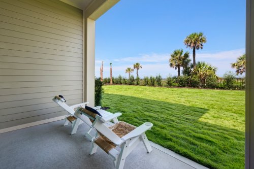 A serene patio with two lounge chairs overlooking a lush green lawn and palm trees under a clear blue sky.