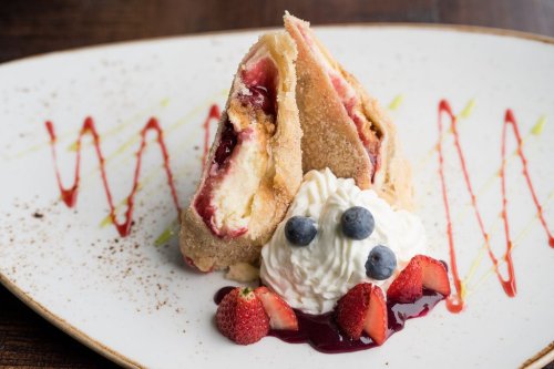 A dessert plate featuring two crispy pastries filled with fruit, accompanied by whipped cream and fresh berries.