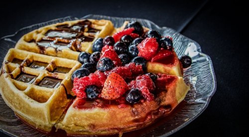 A plate of waffles topped with mixed berries and syrup, served on a glass dish against a dark background.
