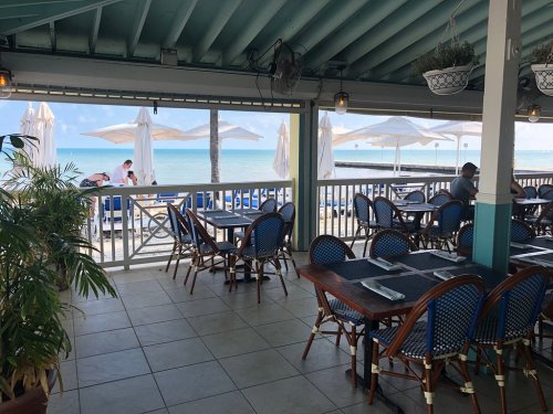 A beachside restaurant with blue decor, empty tables, and umbrellas overlooking the ocean.