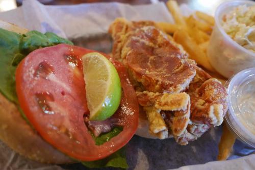 A sandwich with lettuce, tomato, and lime, alongside fried chicken, fries, and two small containers of coleslaw and sauce.