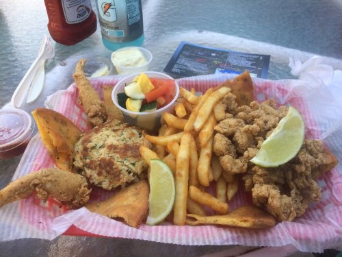 A plate of fried seafood, including crab cakes, fried shrimp, fries, and a side of mixed vegetables with lime wedges.