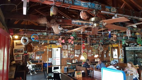 Interior of a rustic restaurant with wooden decor, ceiling fans, and various hanging decorations, including fishing memorabilia.