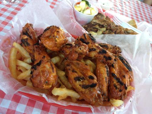 A basket of grilled chicken wings with a spicy glaze, served with French fries and a side of sliced apples.
