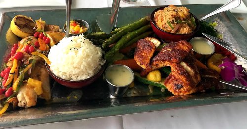 A colorful platter featuring grilled chicken, rice, asparagus, mixed vegetables, and sauces, garnished with an orchid.