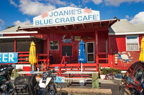 A vibrant red café with a sign reading "Joanie's Blue Crab Café," featuring outdoor seating and colorful umbrellas.