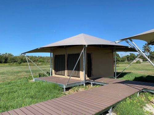 A canvas tent on a wooden platform in a grassy field, under a clear blue sky.