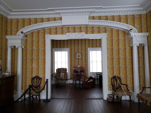 Interior view of a room with yellow patterned wallpaper, white columns, and vintage furniture.