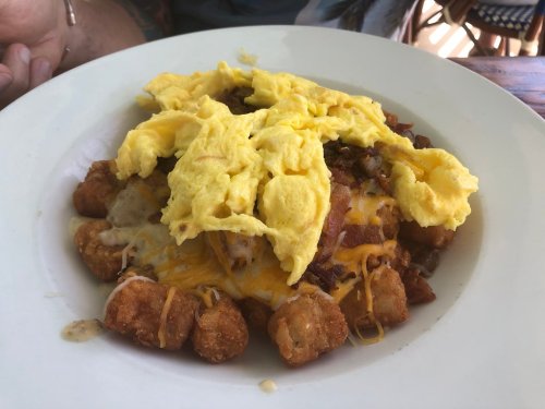A plate of loaded tater tots topped with scrambled eggs, cheese, and bacon.