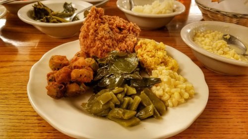 A plate of fried chicken with collard greens, okra, corn, and cornbread, served on a wooden table.