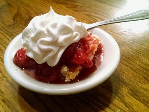 A small bowl of strawberry shortcake topped with whipped cream on a wooden table.