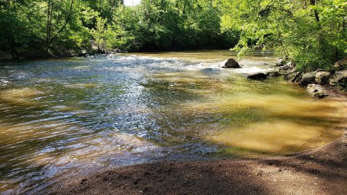 A serene river flows through a lush green landscape, with sunlight reflecting on the water's surface.