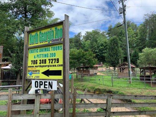 Sign for North Georgia Zoo featuring "Exotic Animal Tours & Petting Zoo," with an open status and surrounding greenery.