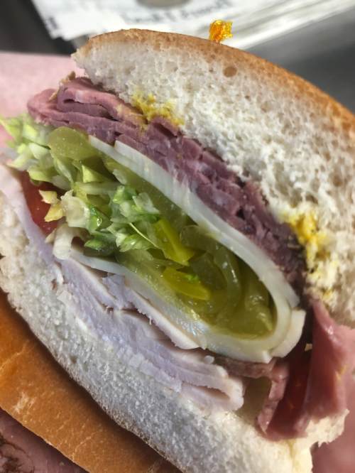 Close-up of a sandwich with layers of ham, turkey, lettuce, pickles, and mustard on soft white bread.