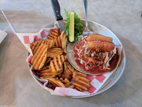 A plate with meatballs topped with sauce and cheese, served with waffle fries and a lime wedge on the side.