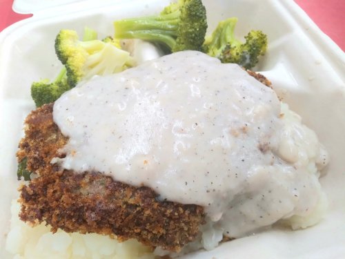 A plate of fried chicken covered in creamy gravy, served with mashed potatoes and steamed broccoli.