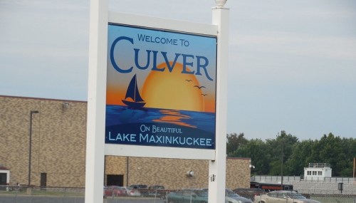 Welcome sign for Culver, featuring a sailboat on Lake Maxinkuckee with a sunset and birds in the background.