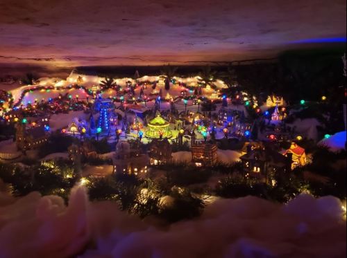 A colorful miniature village scene with lights, snow, and festive decorations, creating a cozy holiday atmosphere.