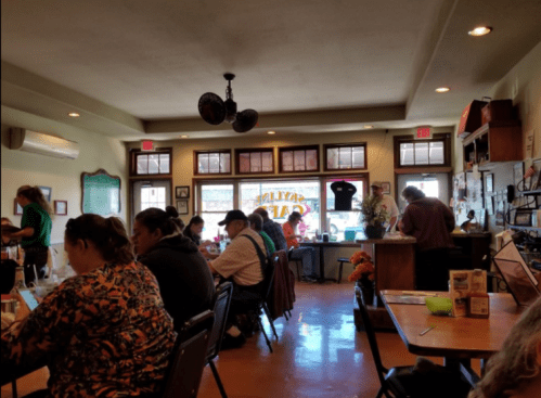 A cozy café interior with patrons dining, a barista at the counter, and bright windows letting in natural light.