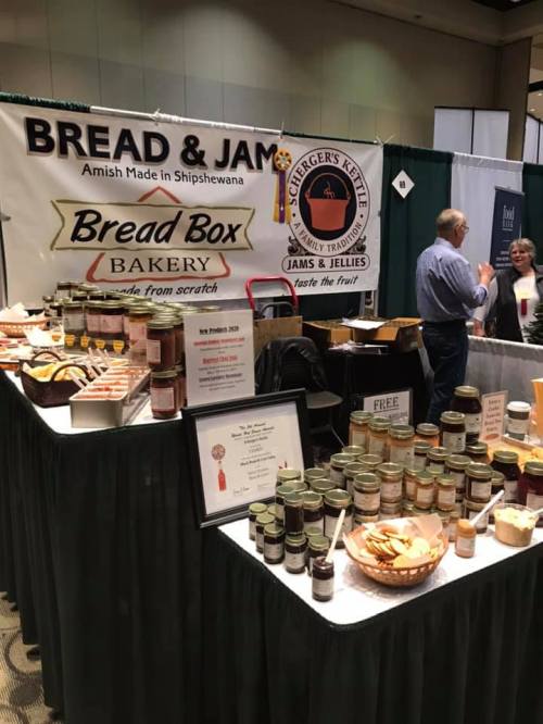 A vendor booth featuring jars of jams and jellies, baked goods, and a sign for Bread Box Bakery at a food event.
