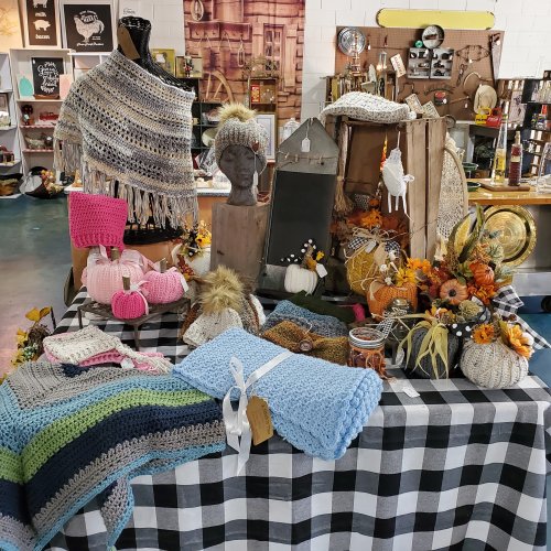 A display of handmade crafts, including knitted items, decorative pumpkins, and autumn-themed decor on a checkered tablecloth.
