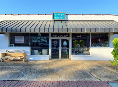 Exterior of the Junque Market storefront, featuring a sign, large windows, and a welcoming entrance.