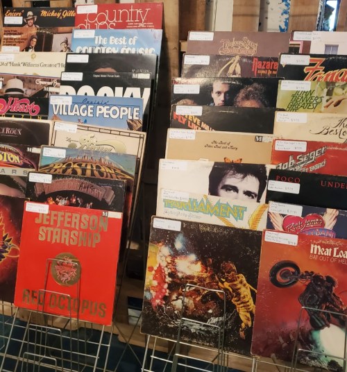 A display of various vinyl records, featuring colorful album covers and price tags, arranged on a wooden rack.