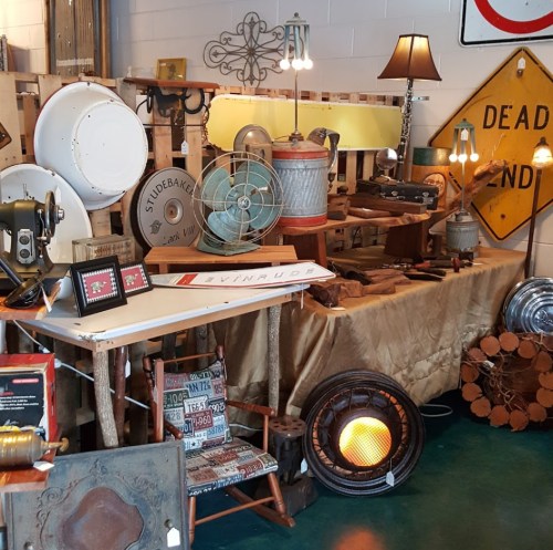 A vintage display featuring various antiques, including fans, lamps, signs, and decorative items on a wooden table.