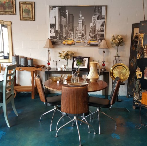 A cozy dining area featuring a round wooden table, chairs, decorative items, and a vintage cityscape artwork on the wall.